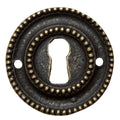 Antique brass keyhole escutcheon with a circular shape and a visible keyhole in the center, surrounded by a decorative beaded edge.
